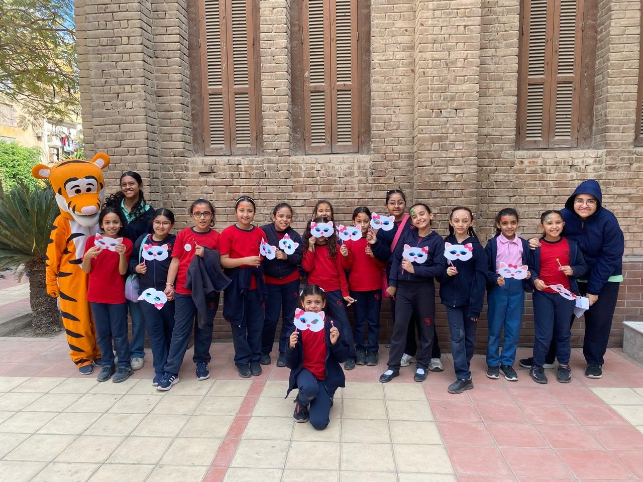 Students with the tiger mascot holding cat masks outside the school